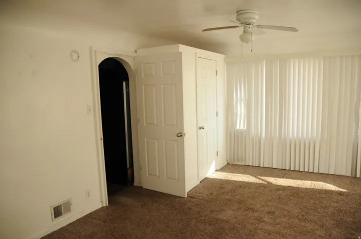Unfurnished bedroom featuring dark carpet, arched walkways, and a ceiling fan