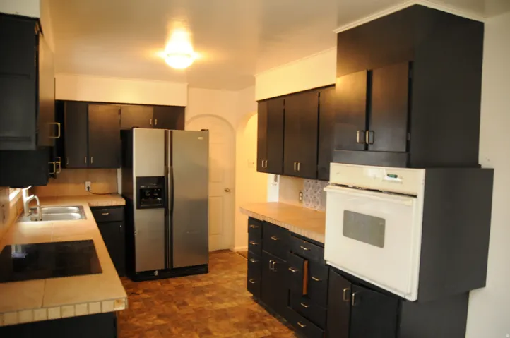 Kitchen with arched walkways, stainless steel refrigerator with ice dispenser, oven, light countertops, and black electric stovetop