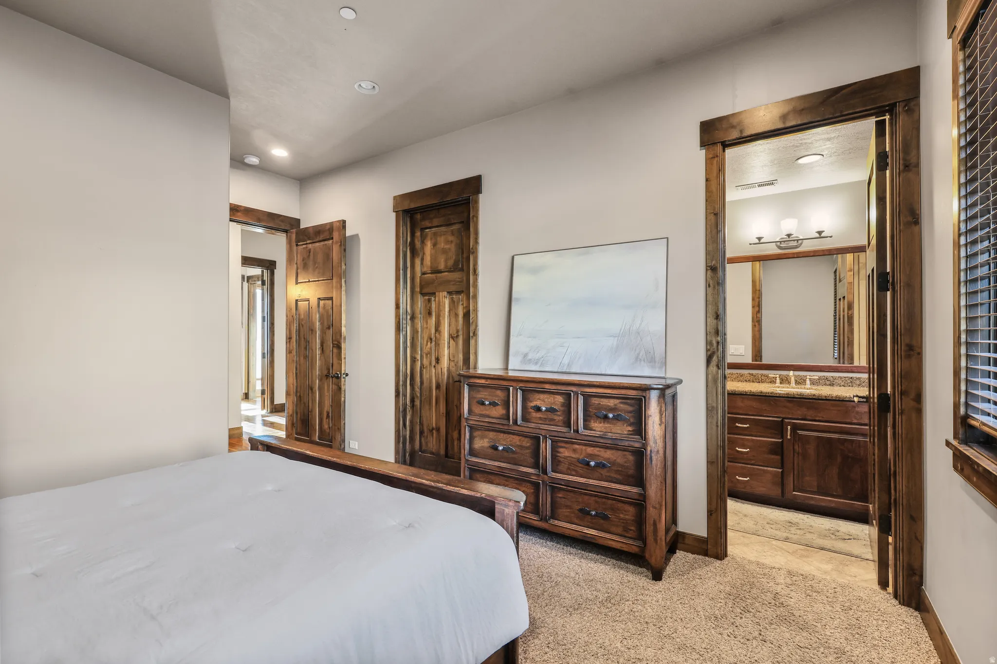 Bedroom with connected bathroom, light colored carpet, and recessed lighting