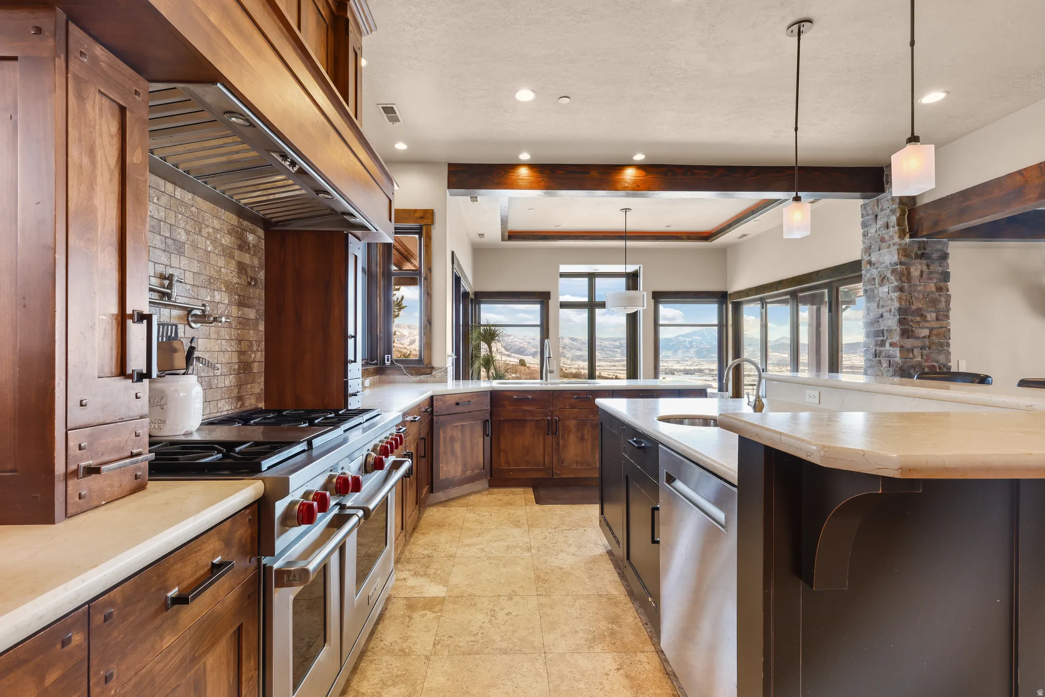 Kitchen featuring stainless steel appliances, decorative light fixtures, a tray ceiling, a center island with sink, and custom exhaust hood