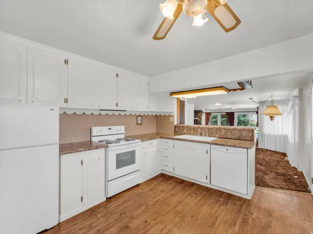 Kitchen with white appliances, white cabinets, a peninsula, and light wood-type flooring