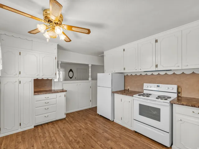 Kitchen featuring white appliances, white cabinetry, dark wood-style flooring, a ceiling fan, and dark stone countertops