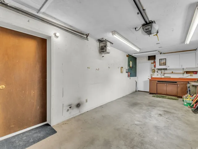 Garage with a workshop area, electric panel, a heating unit, and a garage door opener