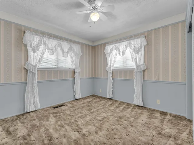 Carpeted spare room with wallpapered walls, a textured ceiling, a ceiling fan, and a wainscoted wall