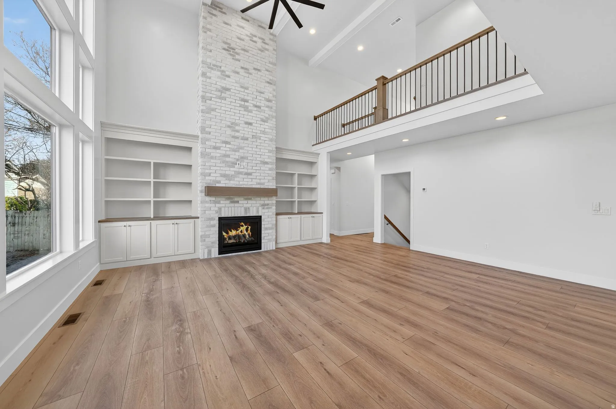 Great room featuring a high ceiling, overlooking balcony, a large fireplace, built in shelves, and light wood-style flooring