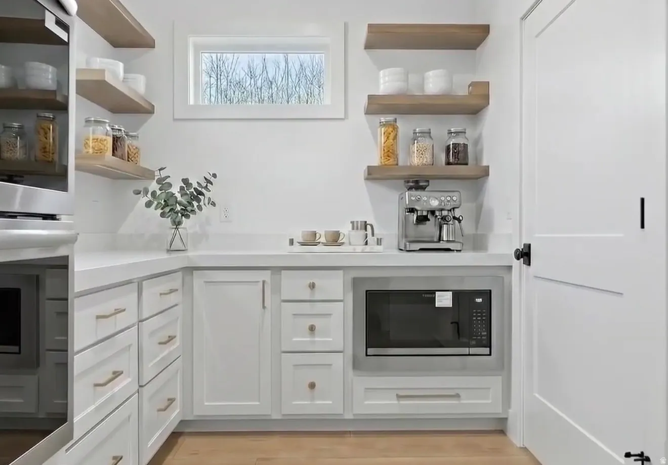 Bar featuring open shelves, white cabinets, stainless steel double oven, built in microwave, and light wood-style floors
