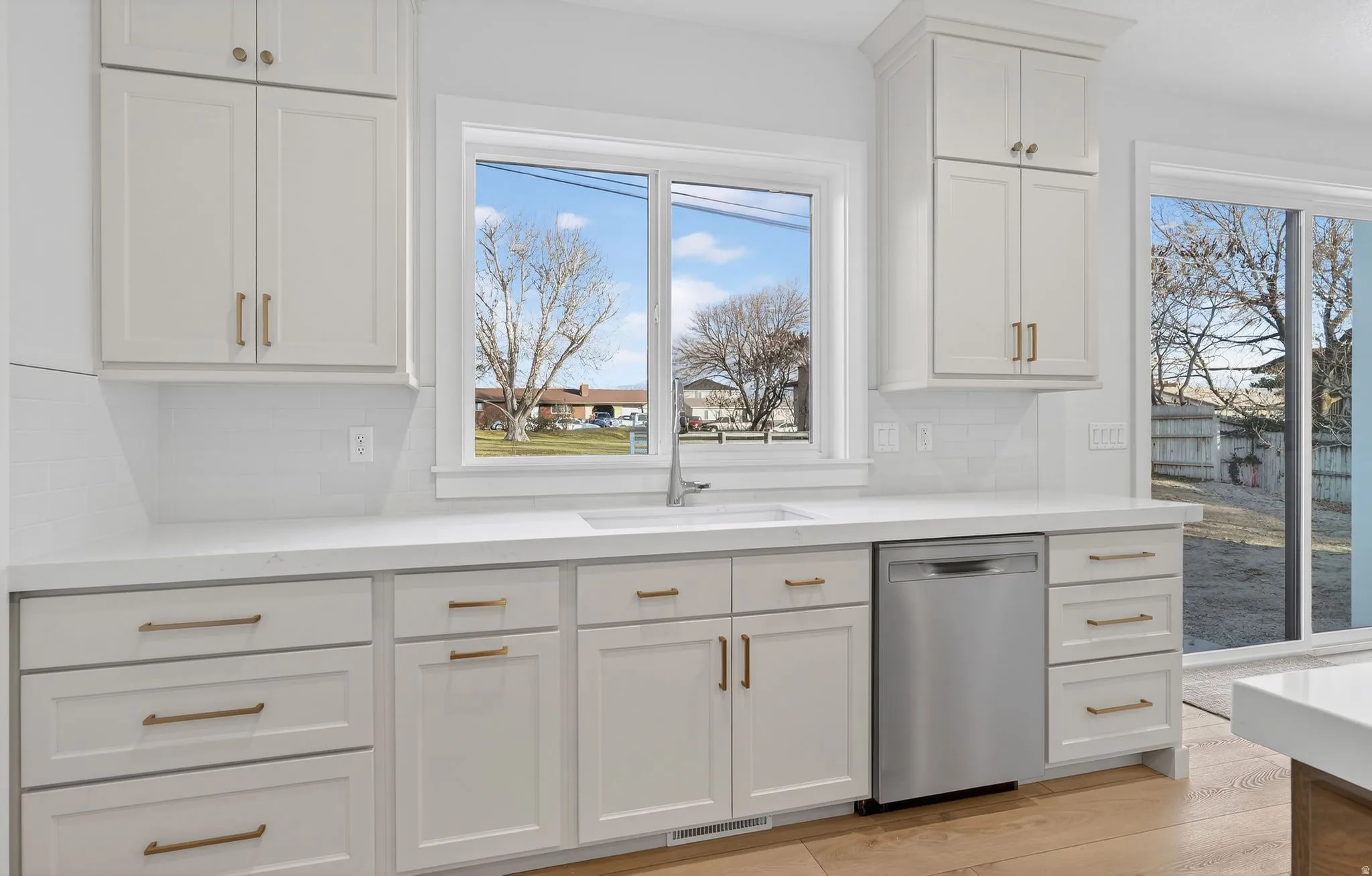 Kitchen with off white cabinets, dishwasher, light wood-type flooring, and light stone countertops and farmhouse sink