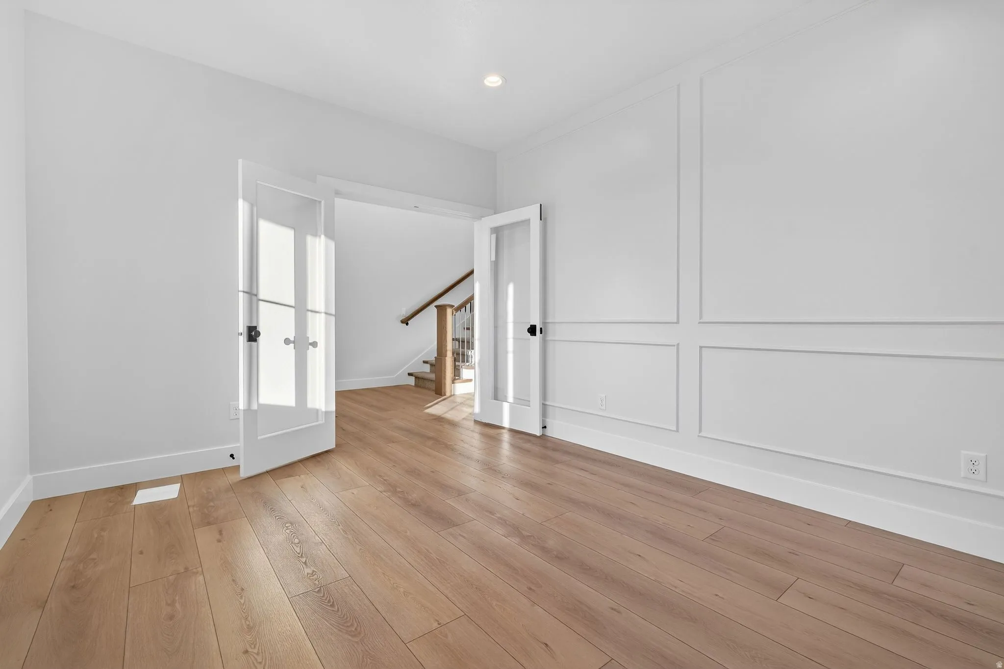 offic or living room with stairway, a decorative wall, light wood-style flooring, and french doors