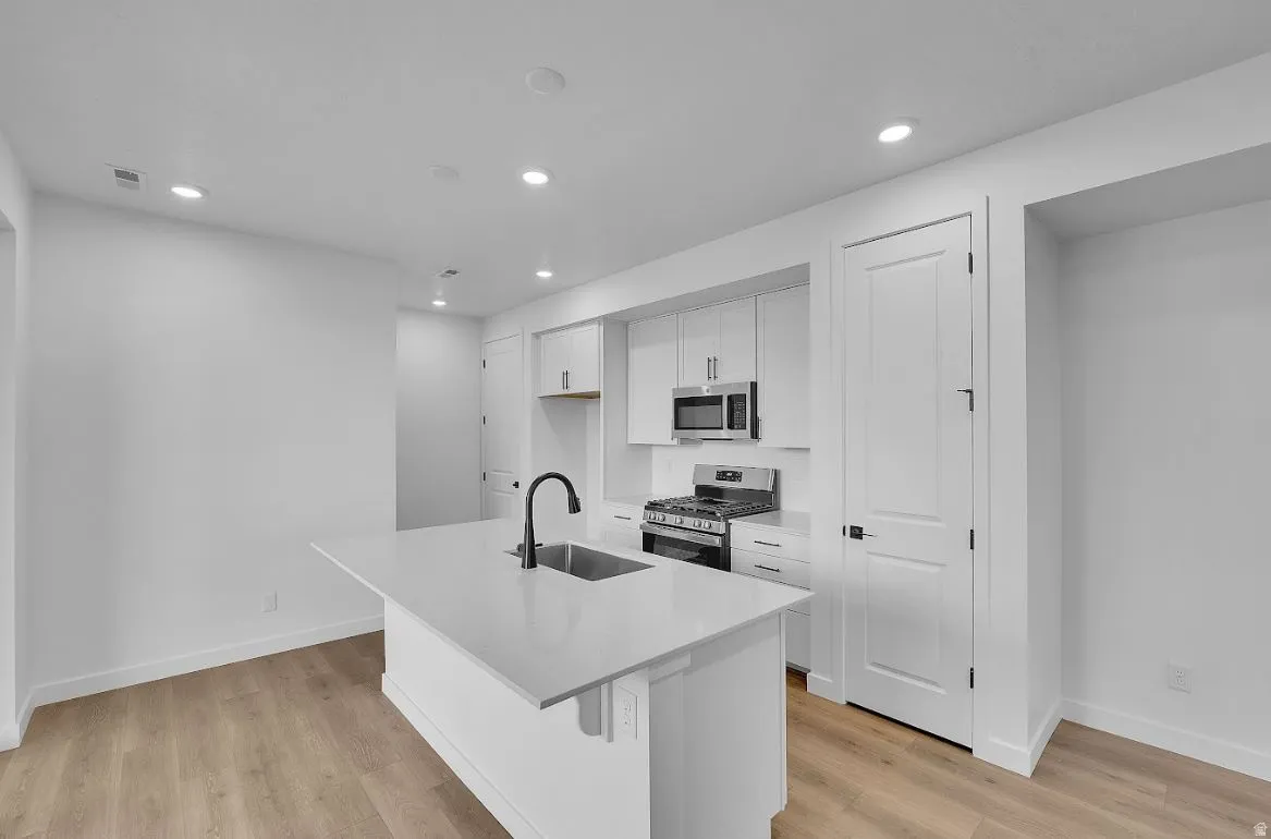 Kitchen with white cabinets, appliances with stainless steel finishes, a center island with sink, recessed lighting, and light wood-style flooring