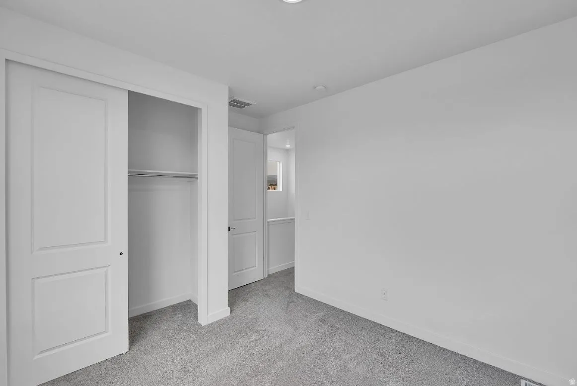 Unfurnished bedroom featuring light carpet and a closet