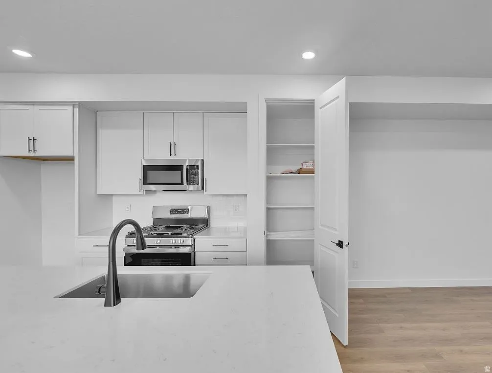 Kitchen featuring white cabinetry, stainless steel appliances, light wood-style flooring, light stone countertops, and recessed lighting