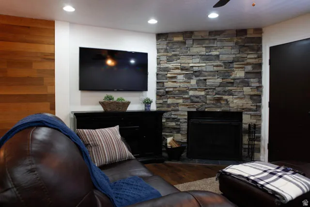 Living room featuring a stone fireplace, ceiling fan, wood finished floors, and recessed lighting