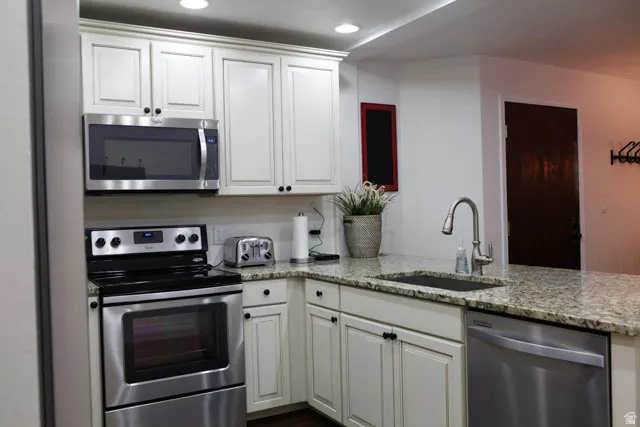 Kitchen with appliances with stainless steel finishes, light stone countertops, white cabinets, and recessed lighting