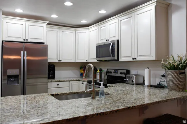 Kitchen with stainless steel appliances, light stone countertops, white cabinetry, recessed lighting, and a kitchen bar