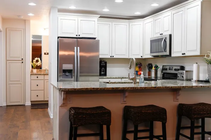 Kitchen with stainless steel appliances, dark stone countertops, a peninsula, white cabinets, and recessed lighting
