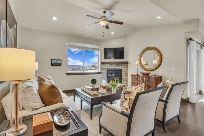 Living room with vaulted ceiling, recessed lighting, a stone fireplace, ceiling fan, and dark wood-style floors