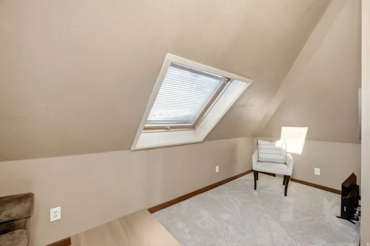 Sloped ceiling room featuring an operable skylight with integrated blinds, light gray carpet flooring, and a baseboard trim