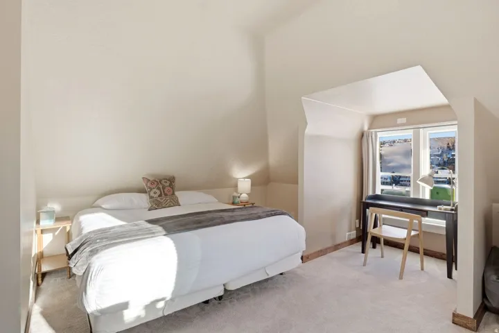 Carpeted bedroom with sloped ceilings, recessed window area, and neutral wall tones