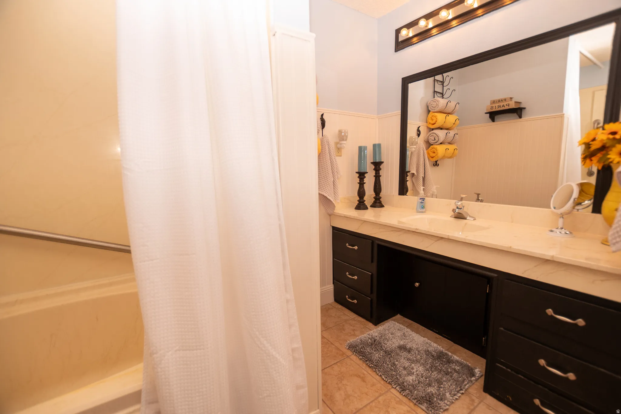 Bathroom featuring vanity, shower / bathtub combination with curtain, a wainscoted wall, and light tile patterned flooring