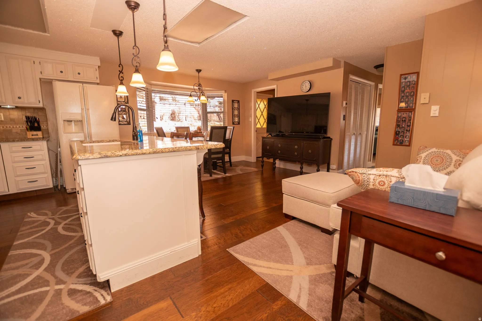 Kitchen with decorative light fixtures, a textured ceiling, light stone counters, dark wood-type flooring, and white refrigerator with ice dispenser