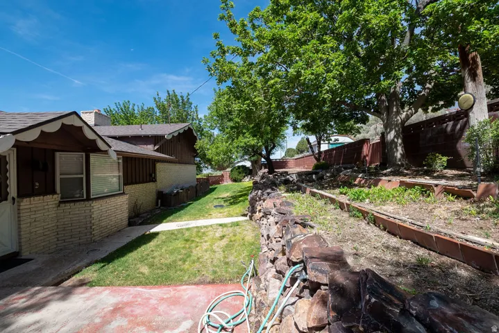 Expansive side yard featuring a manicured lawn, established mature trees, and a stone retaining wall