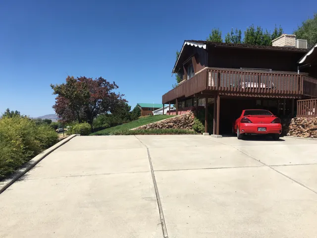 View of side of property featuring concrete driveway, a chimney, a wooden deck, and a carport