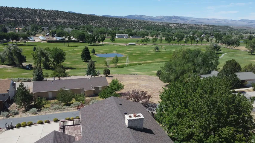 Elevated property perspective offering expansive golf course frontage, mature landscaping, distant mountain ranges, and a structured driveway with a brick-patterned patio