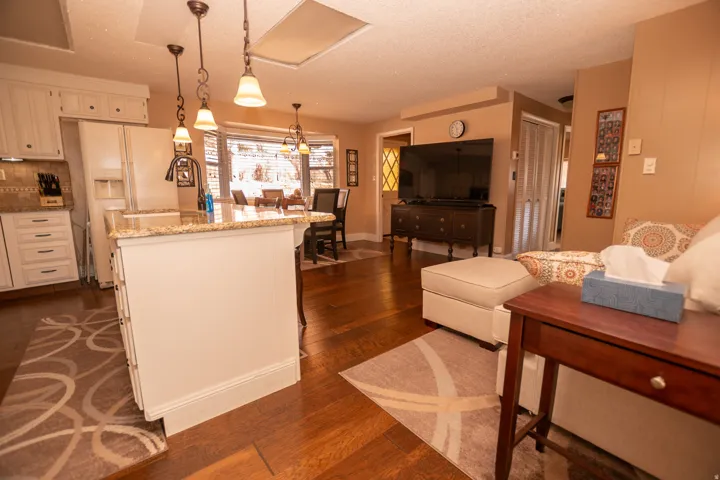 Kitchen with decorative light fixtures, a textured ceiling, light stone counters, dark wood-type flooring, and white refrigerator with ice dispenser