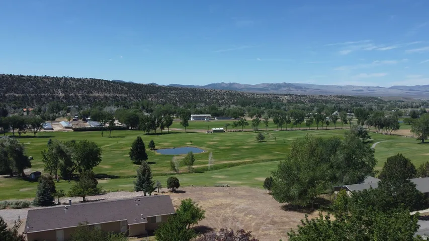 Expansive green landscape featuring a golf course, mature trees, a water feature, and distant hills under a clear sky
