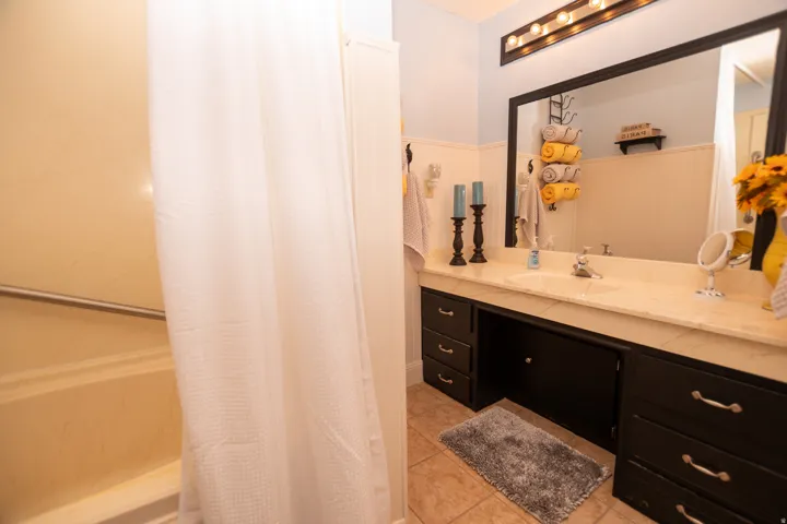 Bathroom featuring vanity, shower / bathtub combination with curtain, a wainscoted wall, and light tile patterned flooring