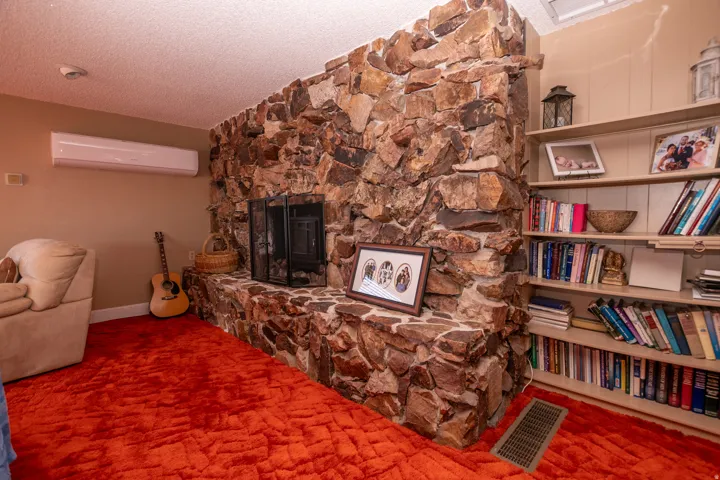 Living area with a textured ceiling, a fireplace, carpet flooring, and a wall mounted AC