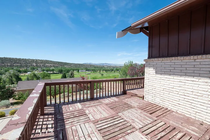 Outdoor deck with wood railing, light-toned brick exterior, and distant verdant landscape