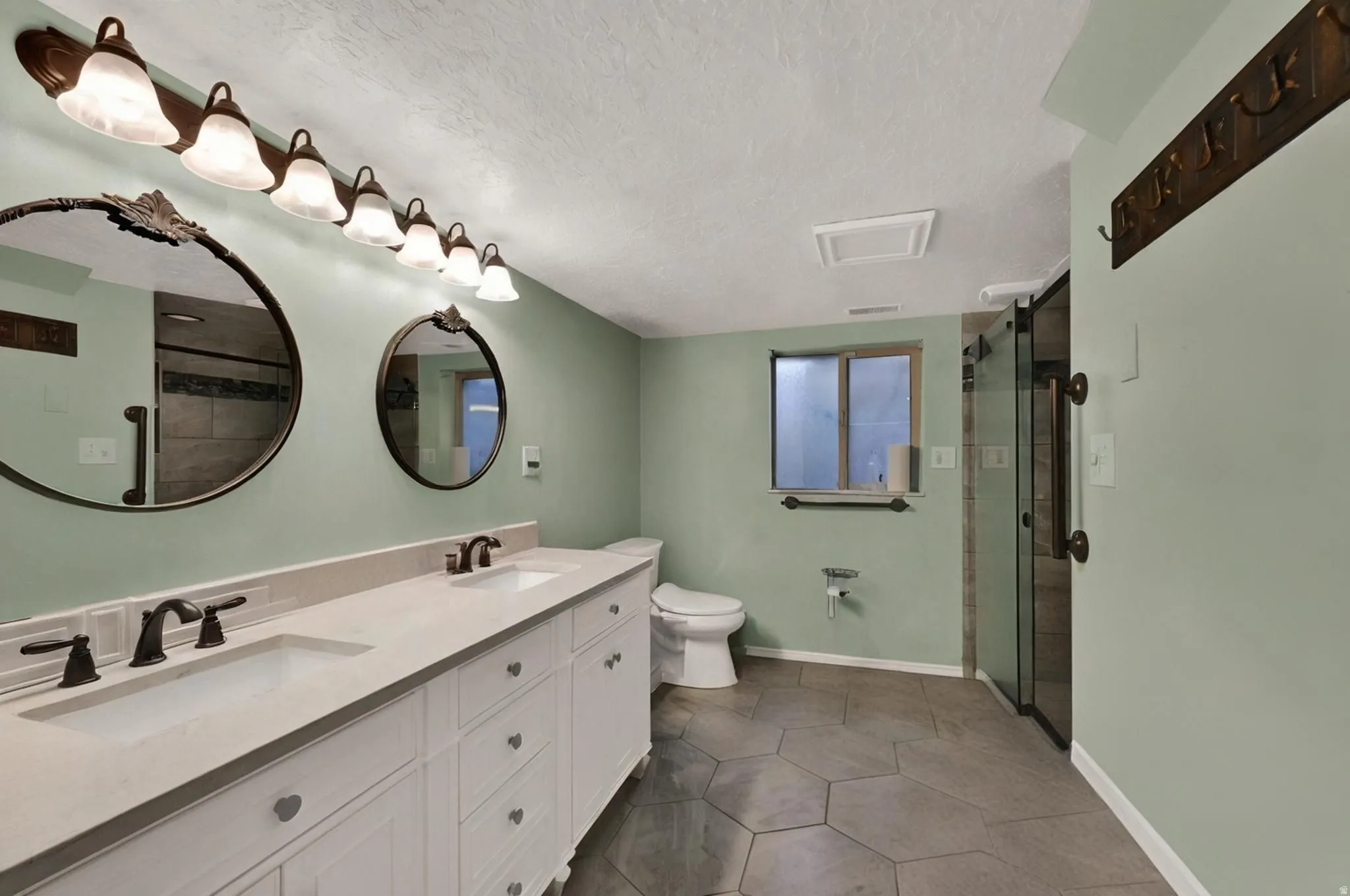 Full bathroom in basement featuring a textured ceiling, double vanity, a shower stall, and dark tile patterned flooring