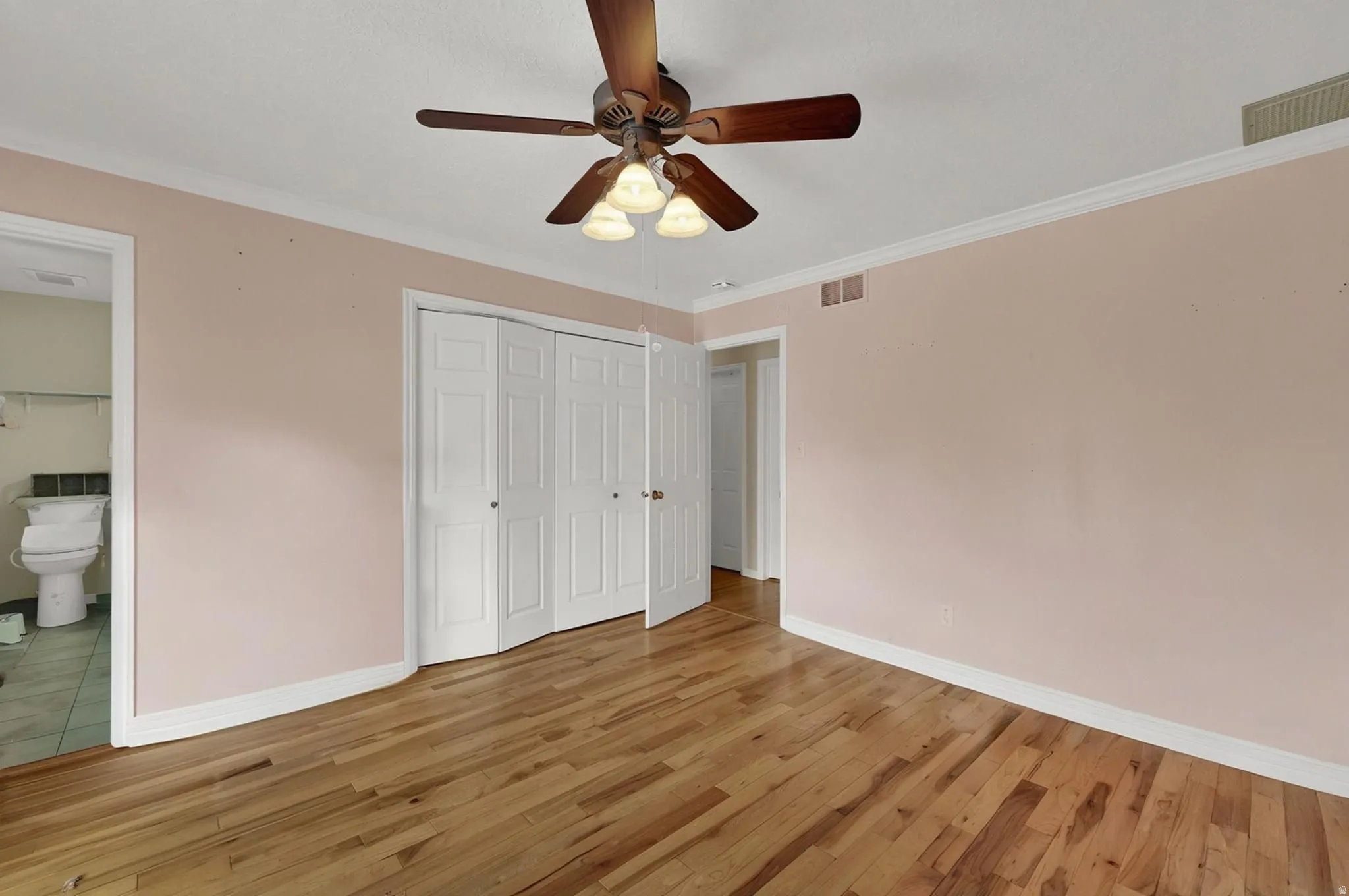 Primary bedroom upstairs with crown molding, light wood-style floors, a closet, a ceiling fan, and connected bathroom