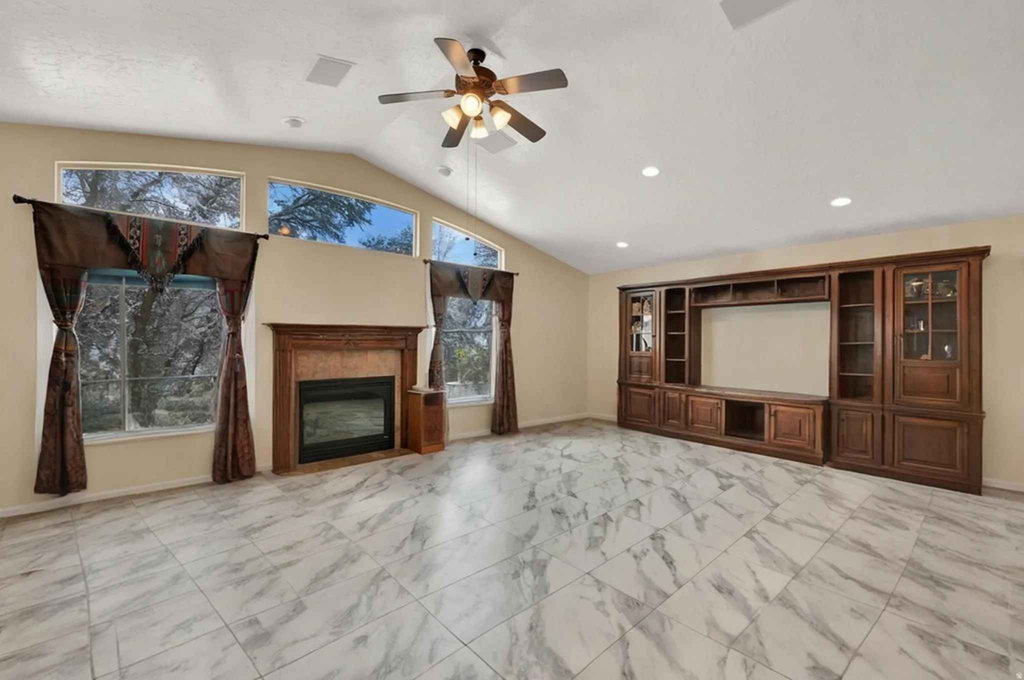 Living room featuring a gas fireplace, light marble finish flooring, a ceiling fan, vaulted ceiling, and recessed lighting