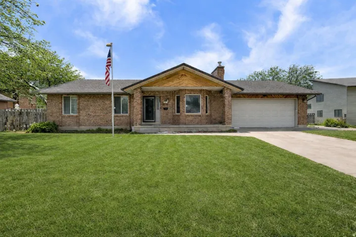 Ranch-style home with a porch, brick siding, a garage, concrete driveway, and a chimney