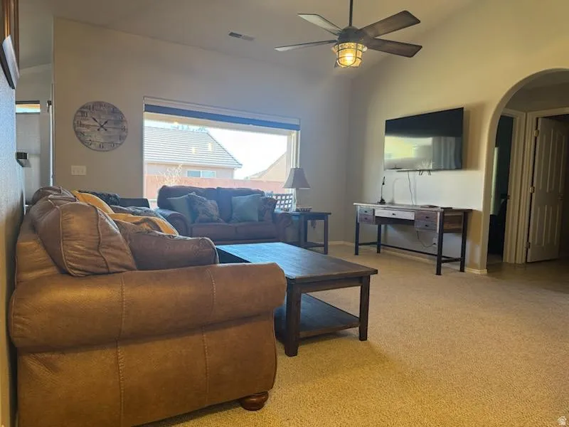 Living area featuring lofted ceiling, arched walkways, light colored carpet, and ceiling fan