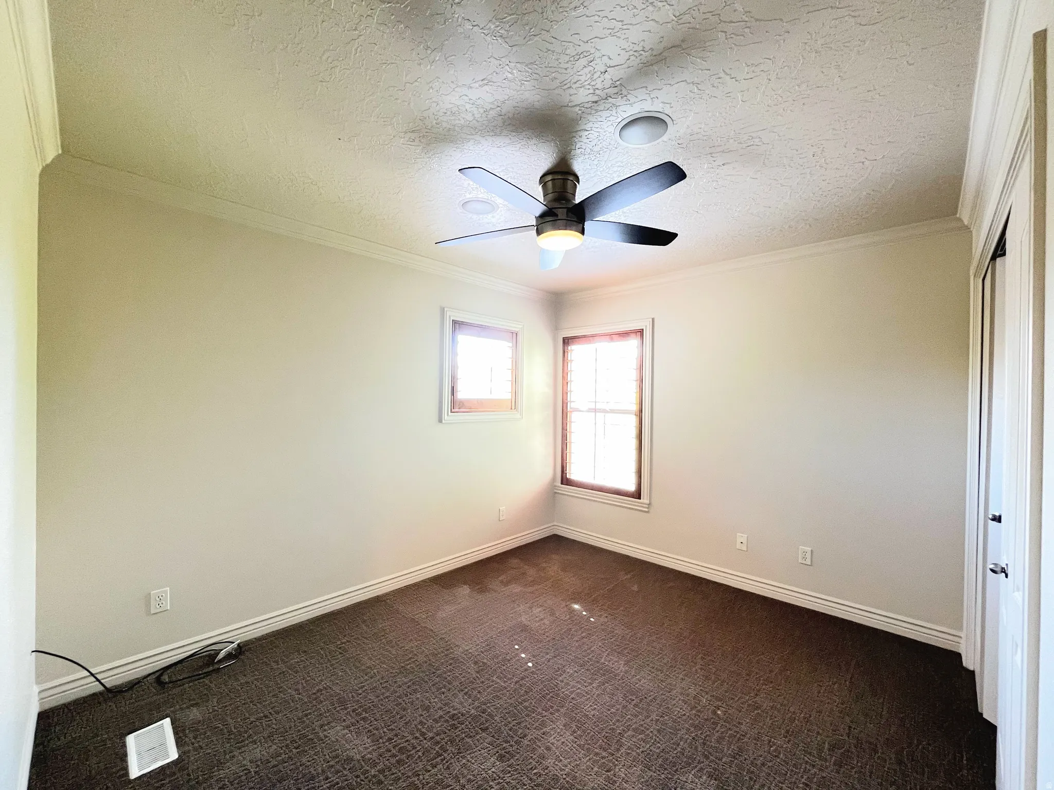 Empty room featuring dark colored carpet, ornamental molding, a textured ceiling, and a ceiling fan