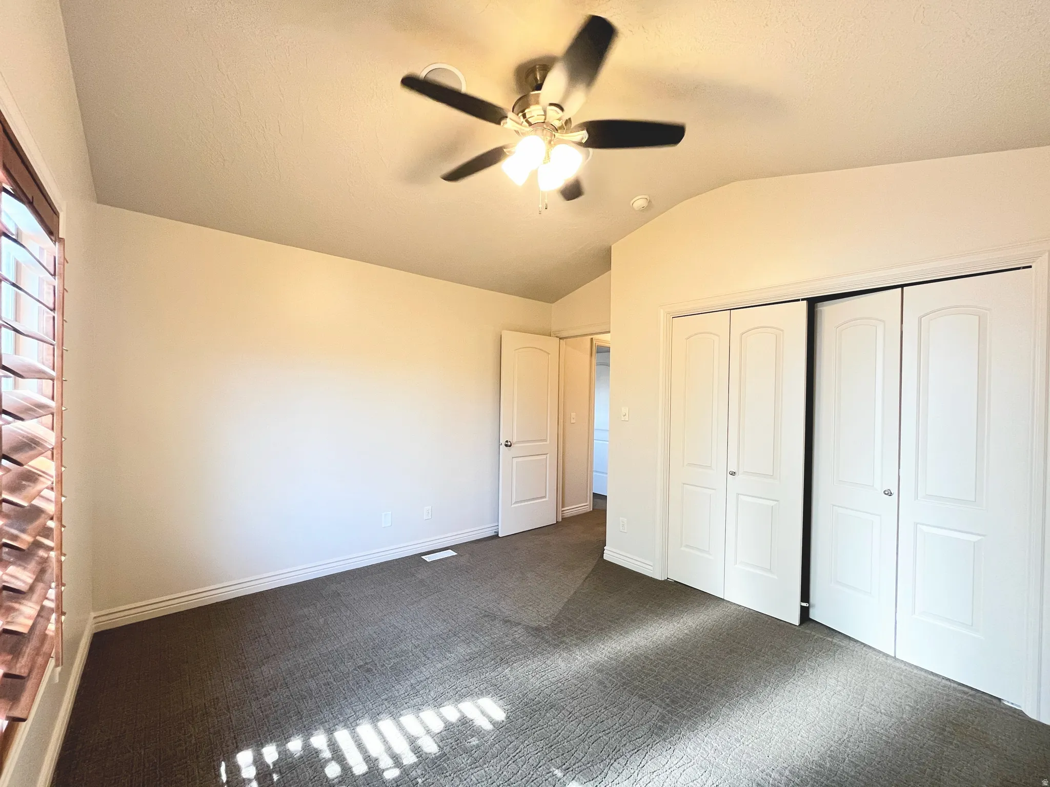 Unfurnished bedroom with dark colored carpet, a ceiling fan, vaulted ceiling, and a closet