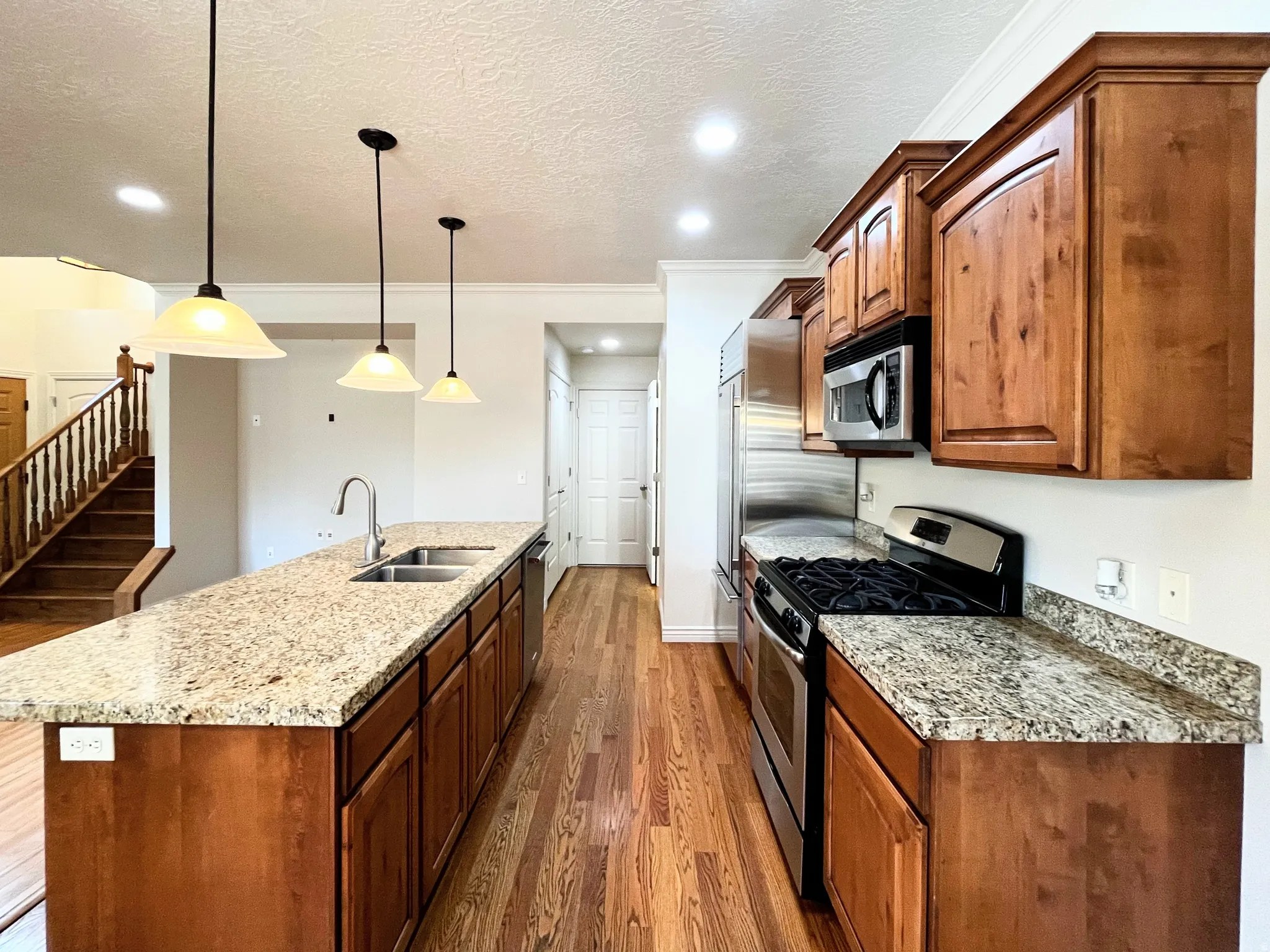Kitchen featuring stainless steel appliances, light stone countertops, dark wood-style flooring, an island with sink, and a textured ceiling