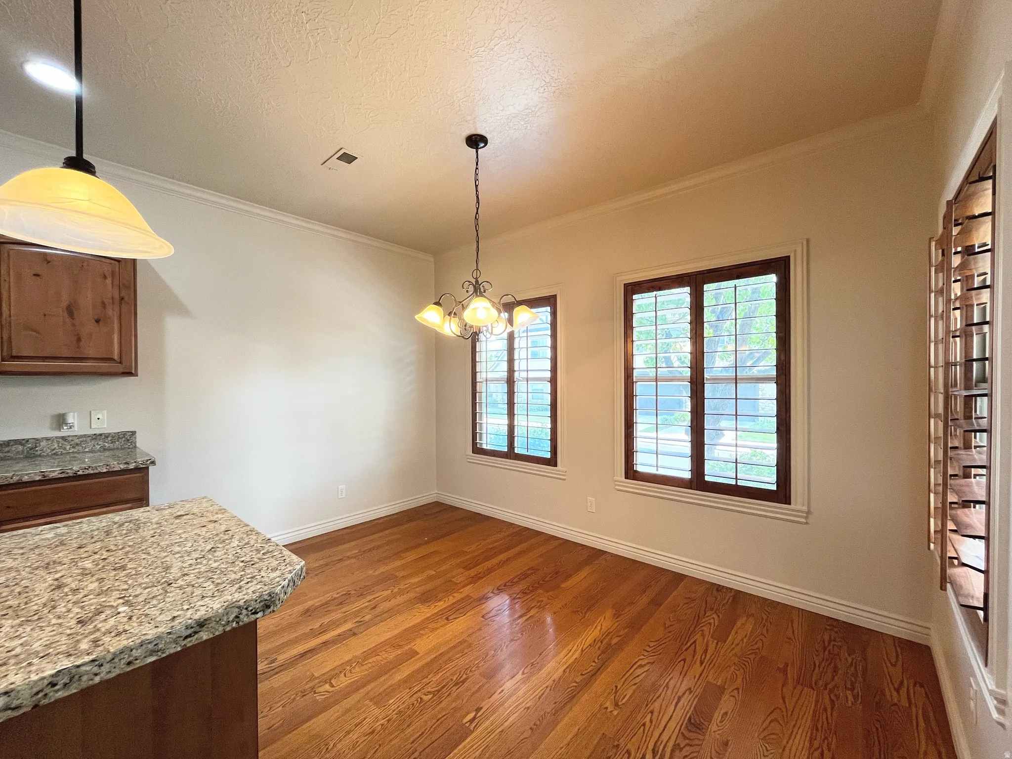 Unfurnished dining area with hanging lights, dark wood-style floors, crown molding, and a textured ceiling