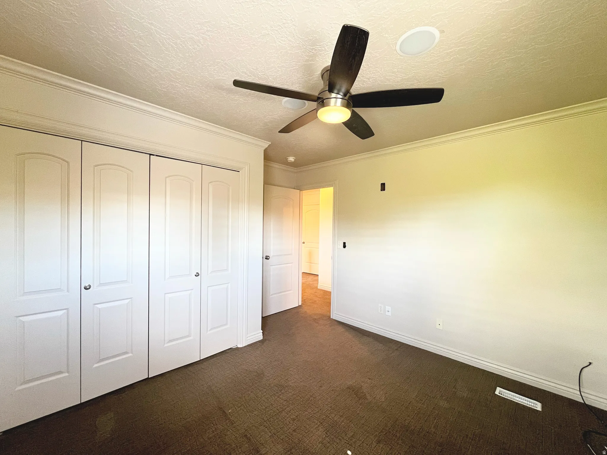 Unfurnished bedroom with crown molding, dark carpet, a closet, a textured ceiling, and a ceiling fan