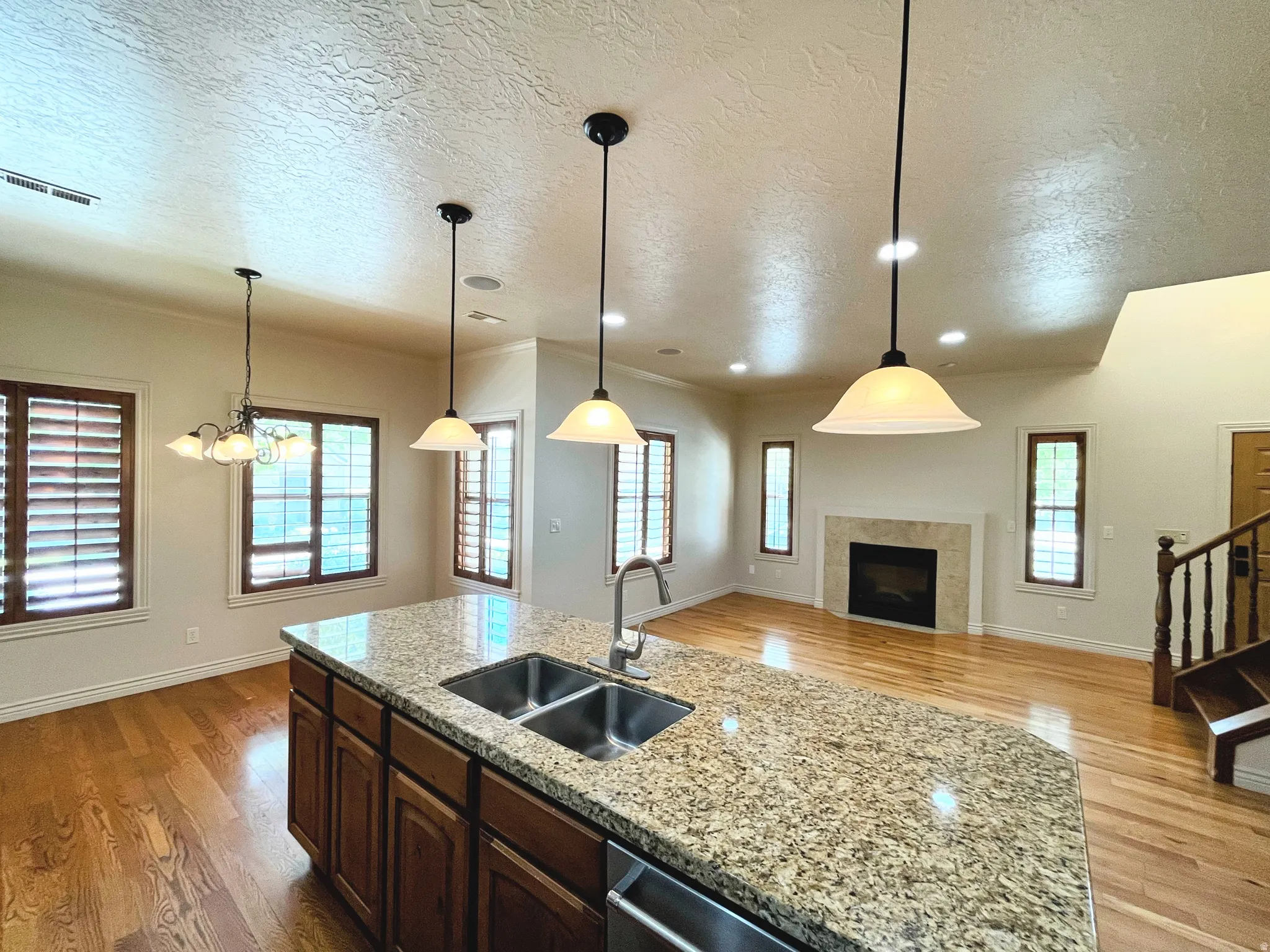 Kitchen with light wood finished floors, an island with sink, a textured ceiling, light stone countertops, and open floor plan
