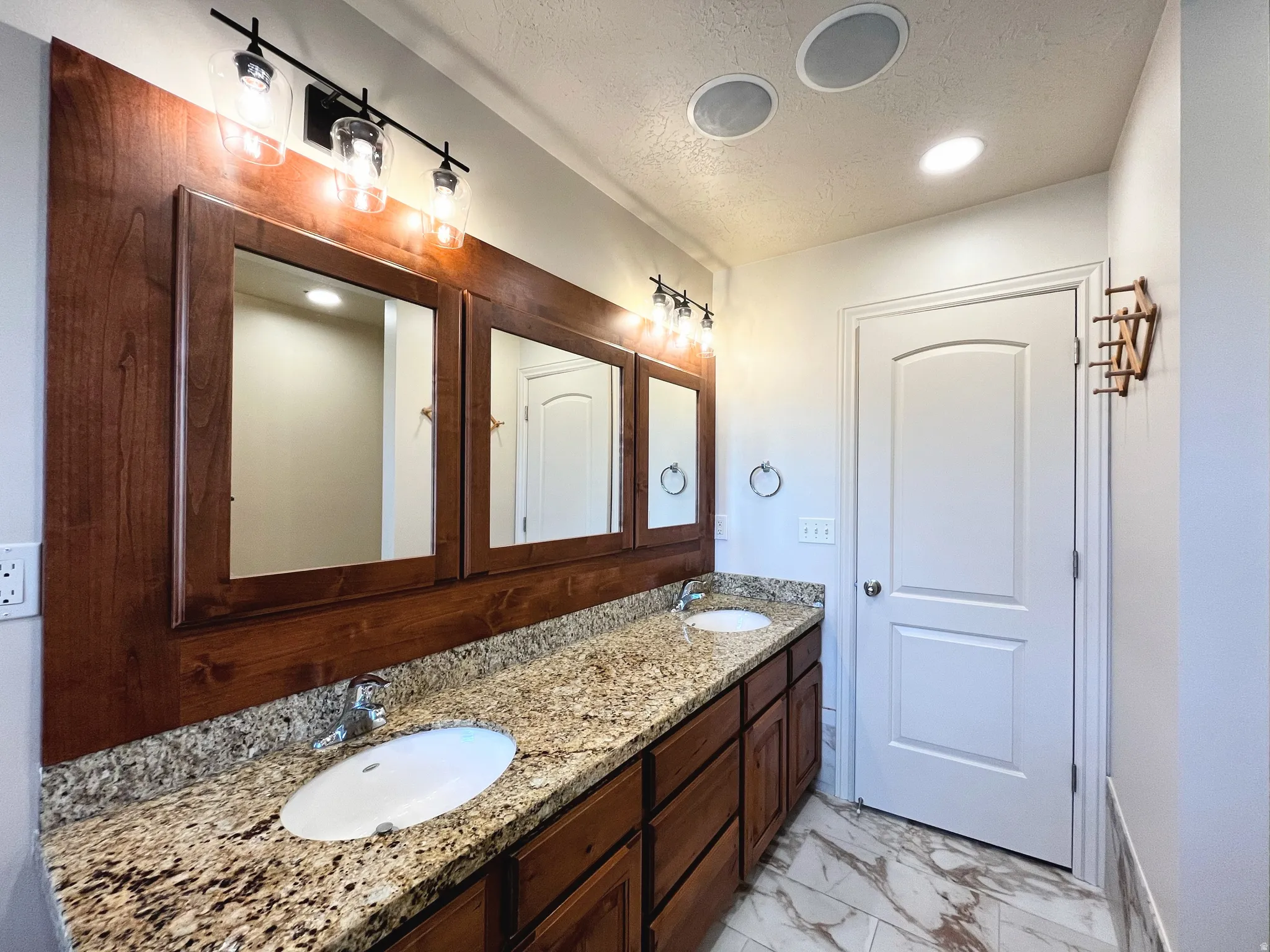 Bathroom with double vanity, a textured ceiling, light marble finish floors, and recessed lighting