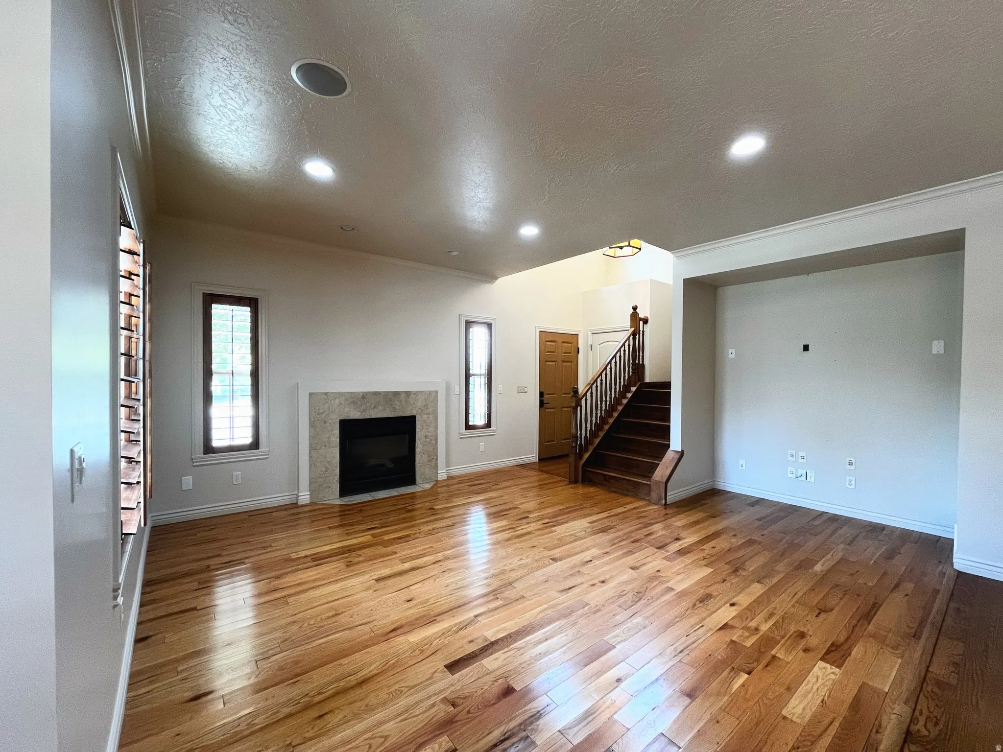 Unfurnished living room featuring light wood-style floors, a textured ceiling, a tiled fireplace, ornamental molding, and recessed lighting