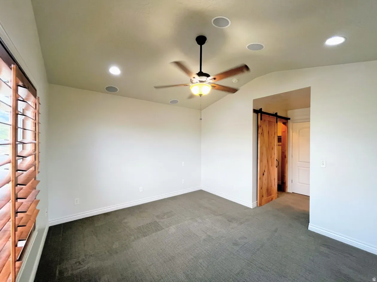 Spare room featuring a barn door, vaulted ceiling, dark colored carpet, ceiling fan, and recessed lighting