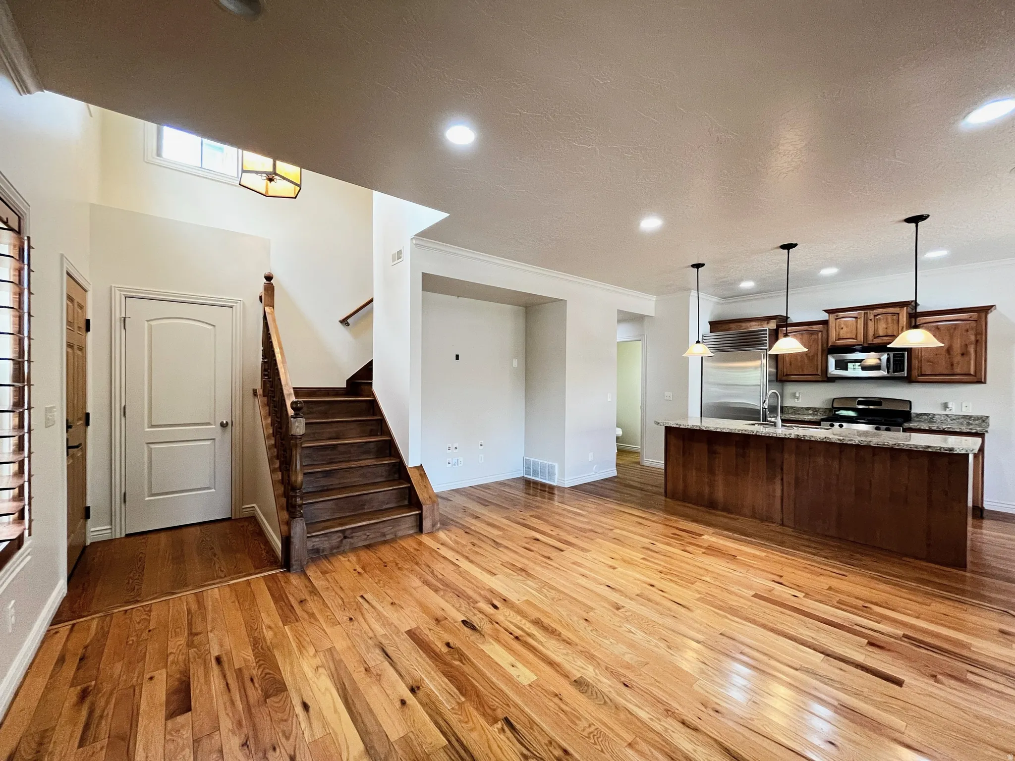 Kitchen with open floor plan, light wood finished floors, light stone counters, hanging light fixtures, and a kitchen island with sink