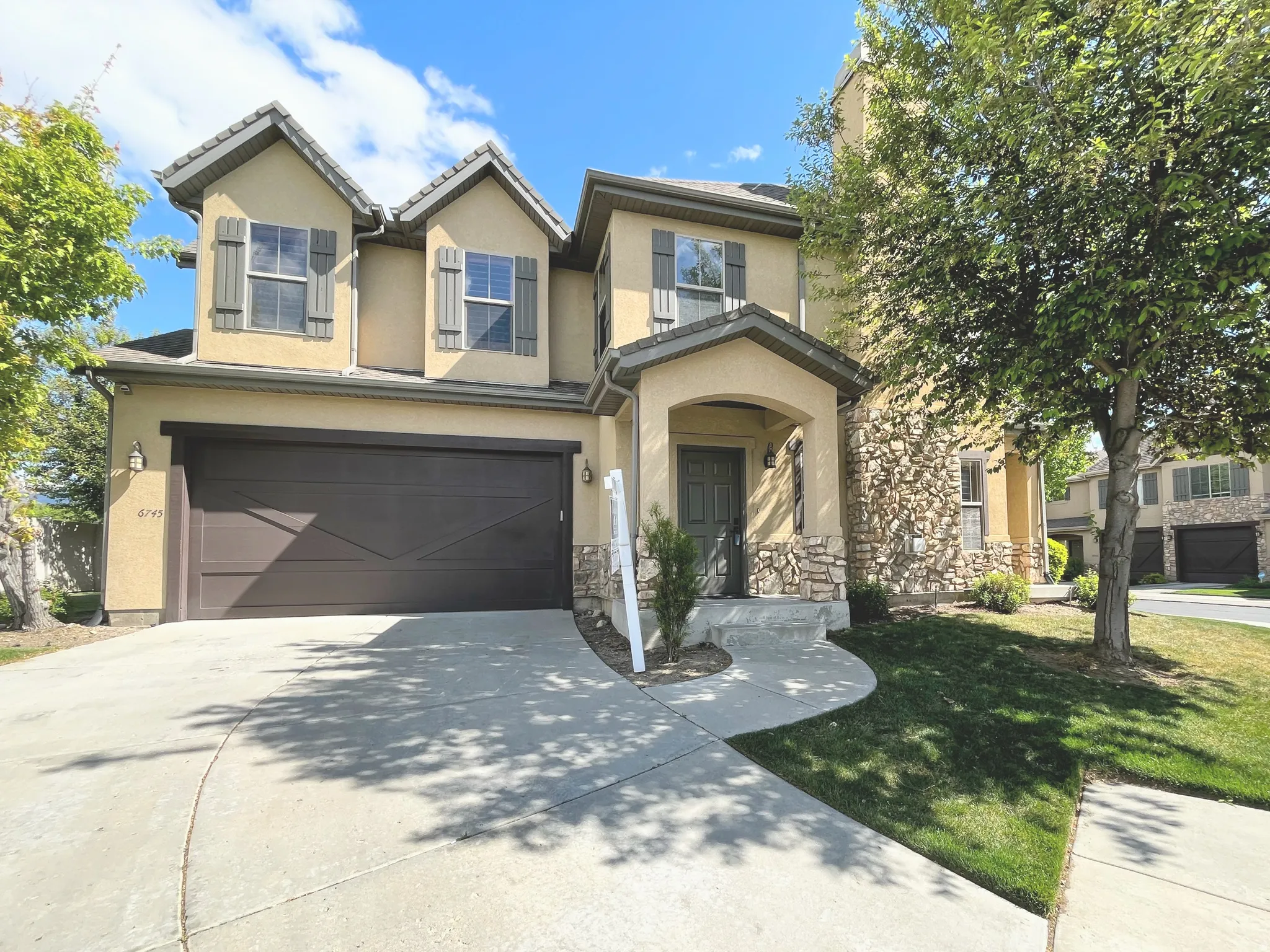 Traditional-style home with driveway, a garage, stucco siding, a front yard, and stone siding