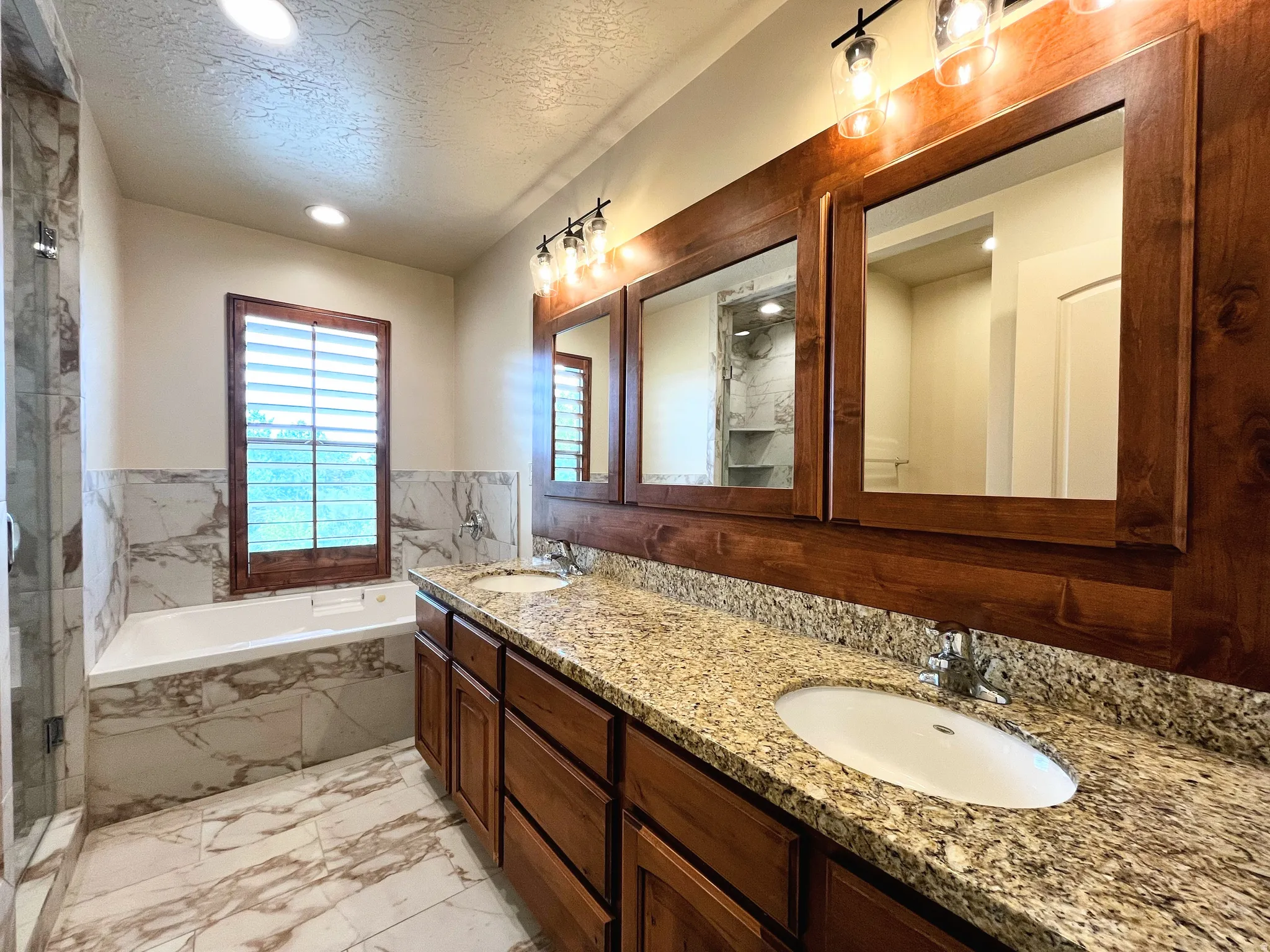 Full bath featuring light marble finish flooring, double vanity, a textured ceiling, a bath, and a marble finish shower
