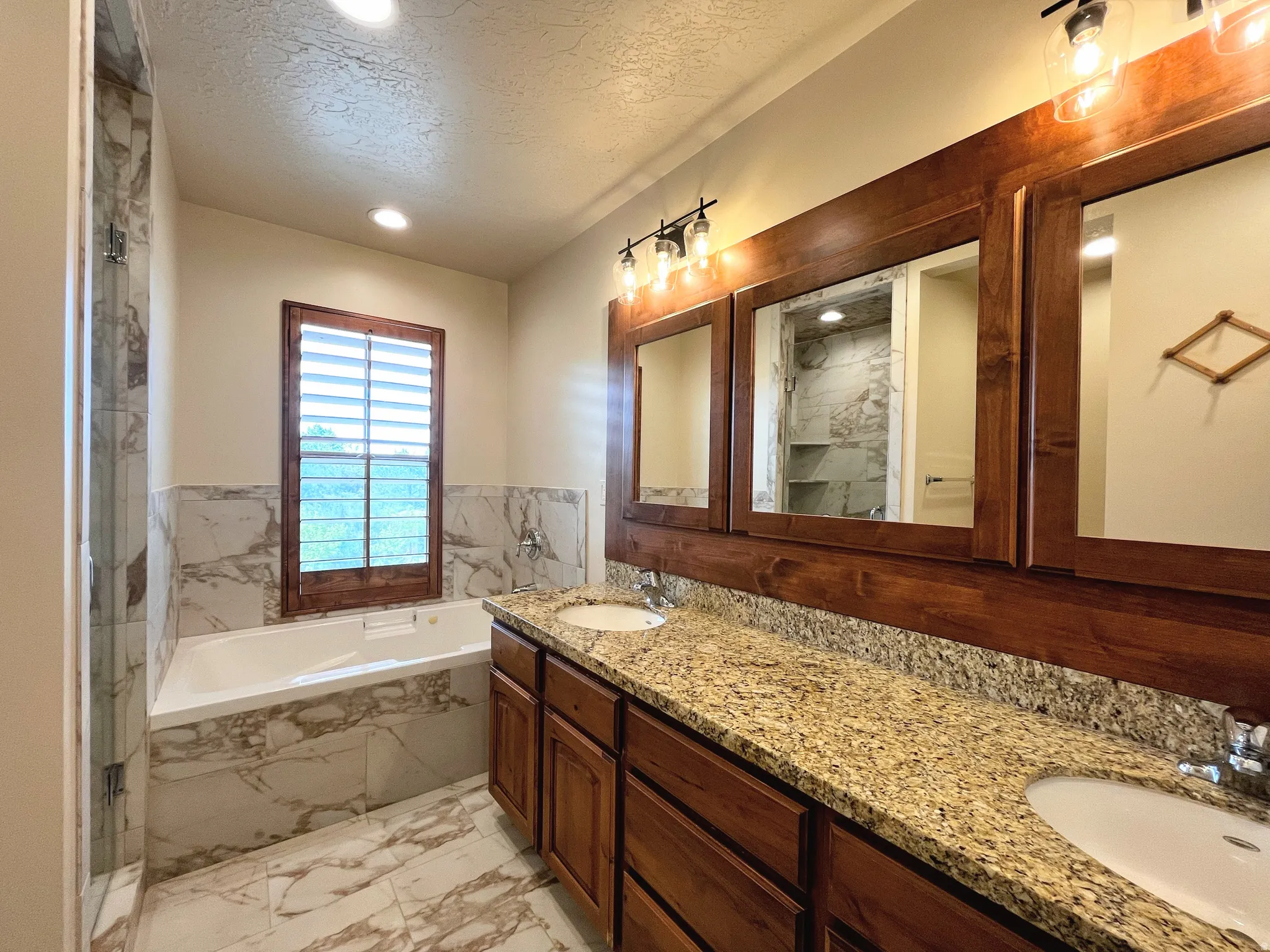 Full bath with light marble finish floors, a textured ceiling, double vanity, a garden tub, and recessed lighting